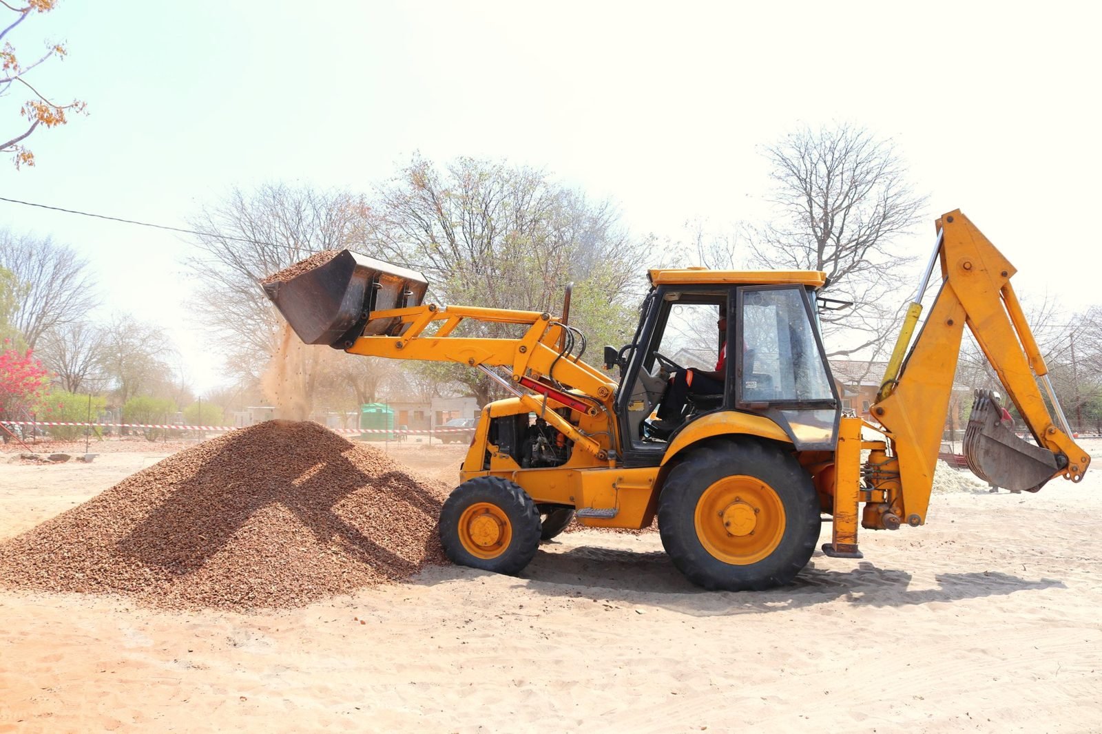 Backhoe loader dumping a bucket of gravel onto a pile