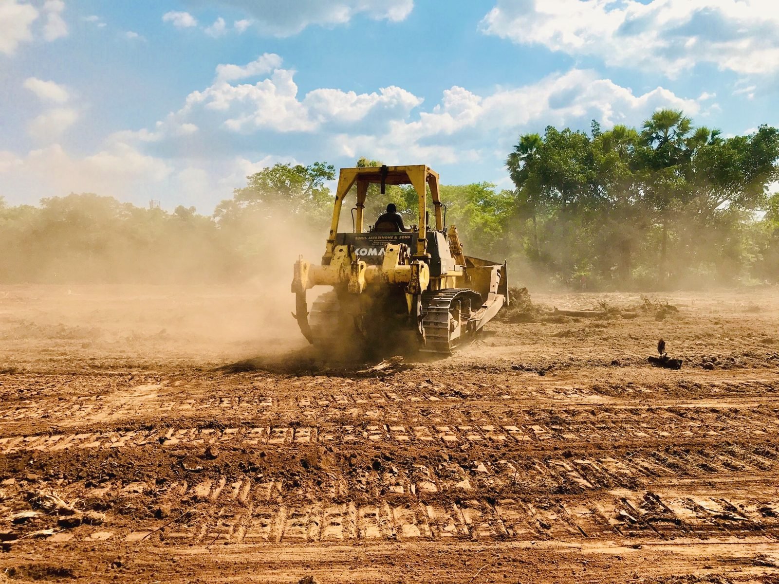 Bulldozer working dry ground with a dust cloud behind