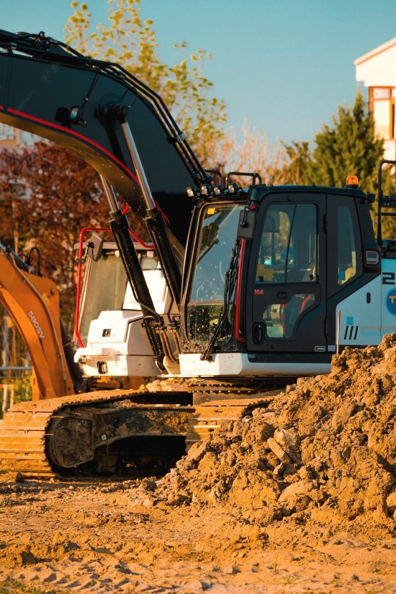Excavator beside piles of dug dirt with trees behind