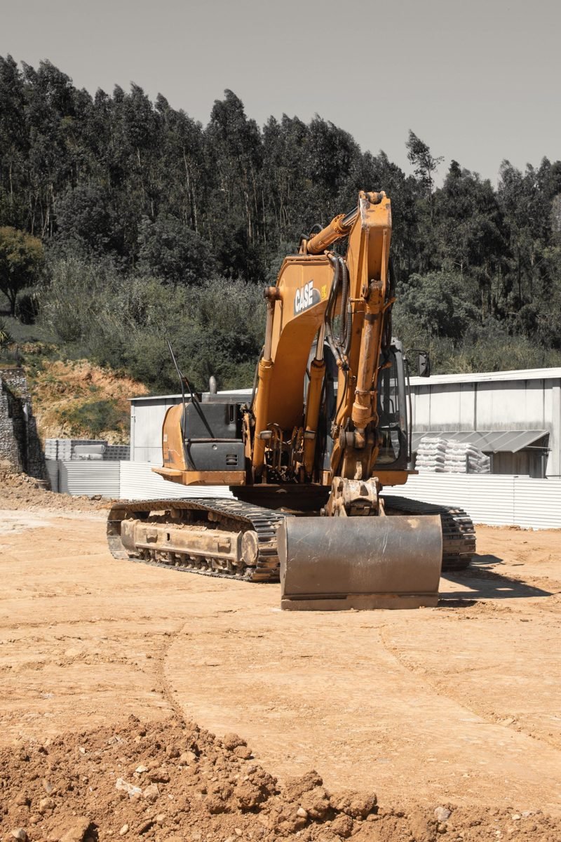 Orange excavator on a bare site with trees behind